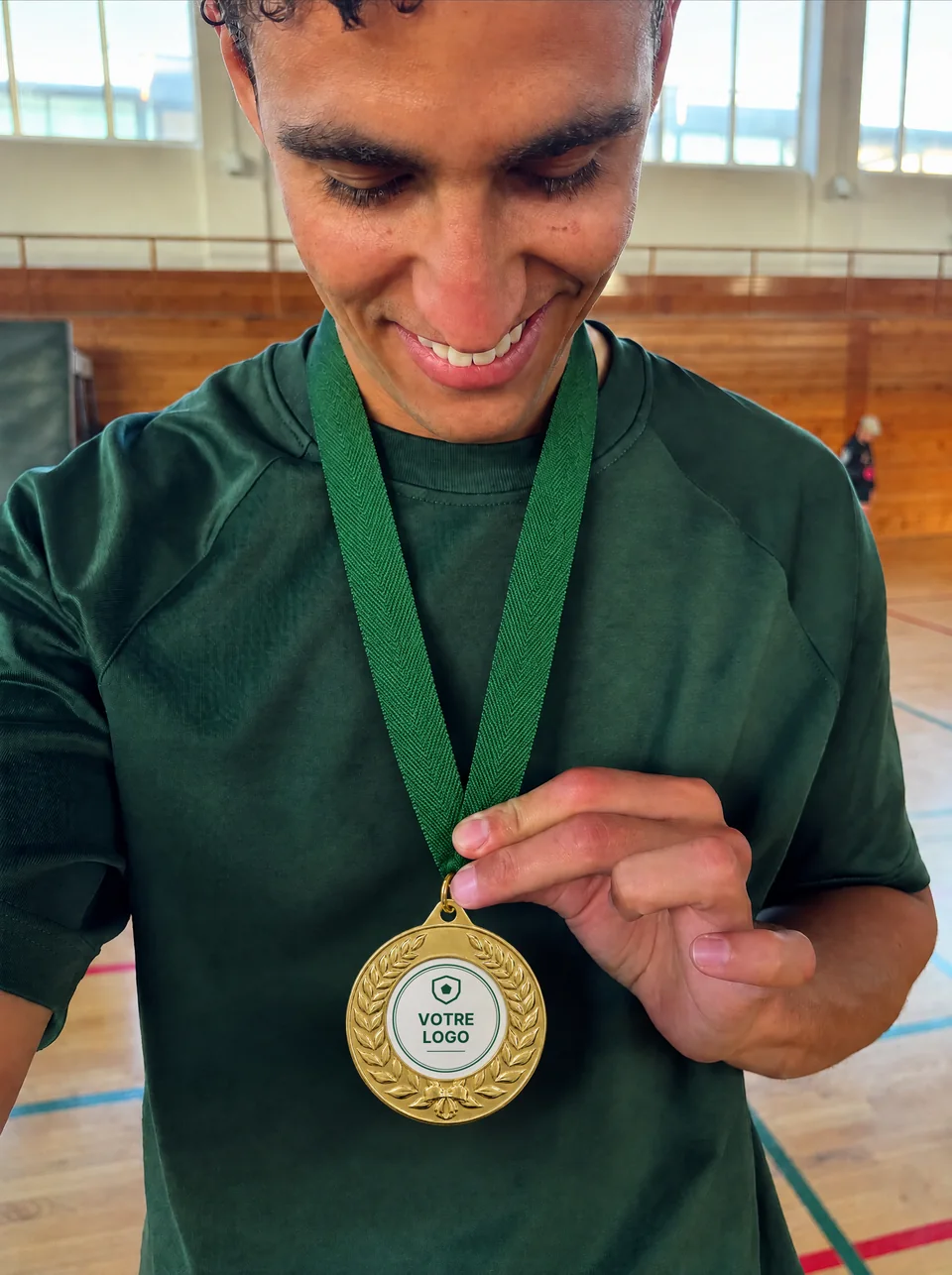 Mise en situation générée : un joueur sourit en montrant sa médaille dorée à couronne de laurier, avec « Votre logo » imprimé au centre.